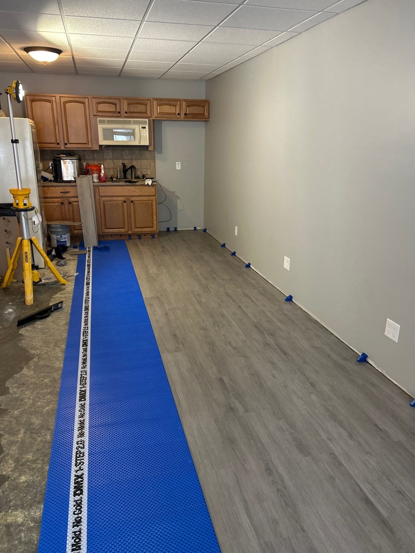 LVP flooring installation in progress with blue underlayment in basement kitchen area