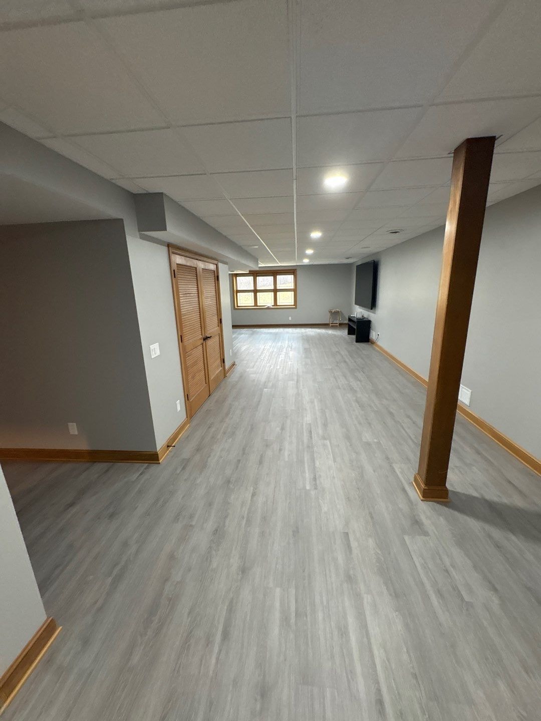 Finished basement with gray LVP flooring, wood trim, and recessed lighting